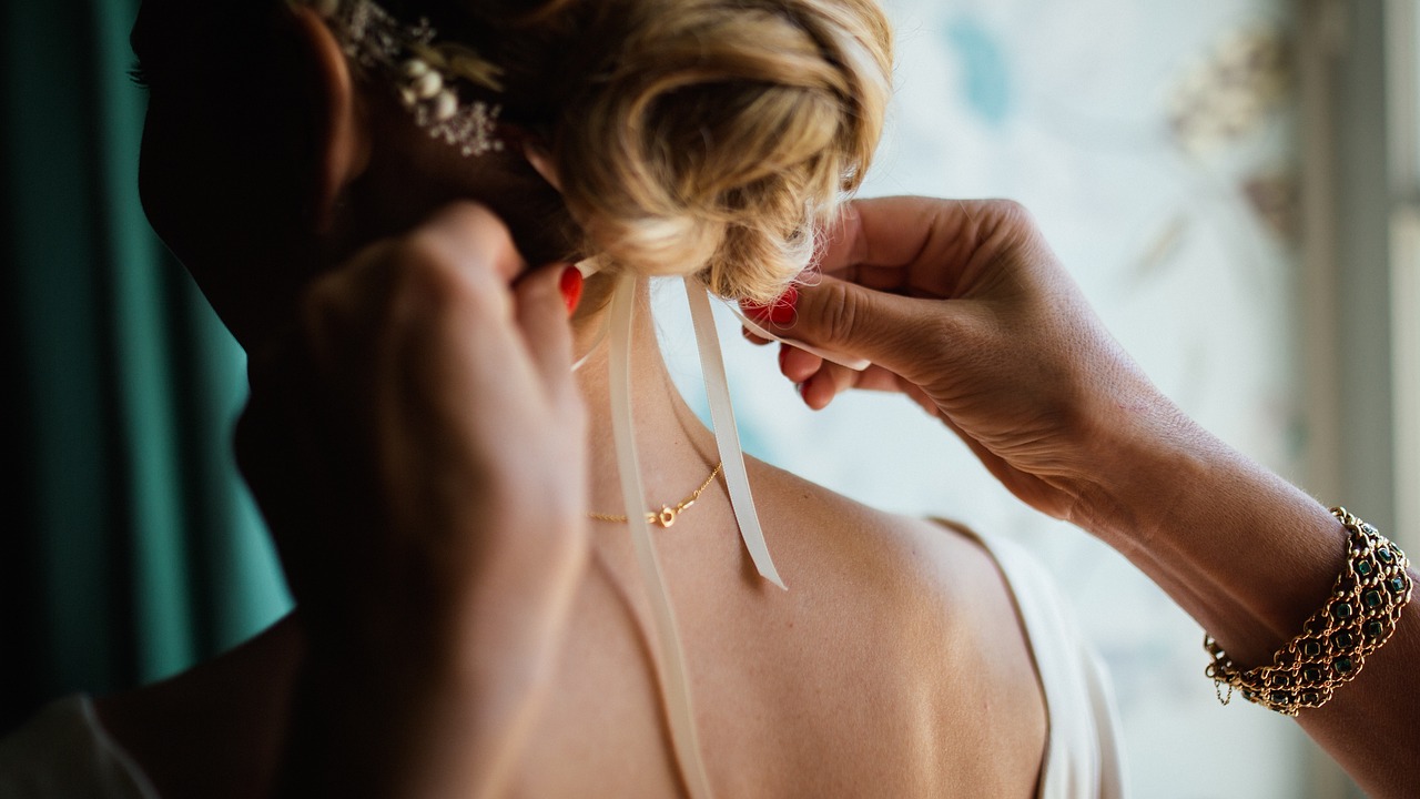 Bride's long hair being styled into an elegant wedding hairstyle by hands of professional hairstylist.