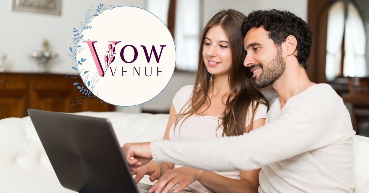 Couple sitting on a couch, engaged in wedding planning as the groom-to-be points at the computer screen. The Vow Venue logo is displayed in the lower left corner of the image.